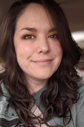 A person with a bright smile and long, wavy hair, dressed in a casual top.