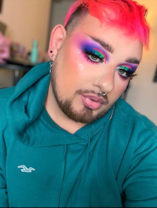 A reviewer with vibrant makeup, featuring bold eyeshadow and contour, casually dressed in a hoodie