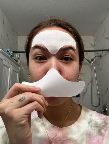 A reviewer applies a facial skincare mask to their forehead