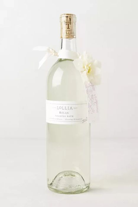 A large glass bottle of Lollia Relax Foaming Bath, complete with a white label, floral tag, and a delicate ribbon tied around it, exuding elegance.