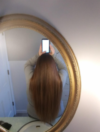 A reviewer with long, straight hair taking a mirror selfie with their smartphone in a bathroom, highlighting their hair.