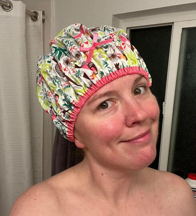 A person sporting a cute patterned shower cap, smiling happily in the bathroom, enjoying their bath time.