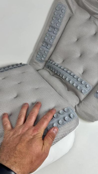 A hand gently resting on a gray massage chair cushion, its textured nodes offering soothing comfort.