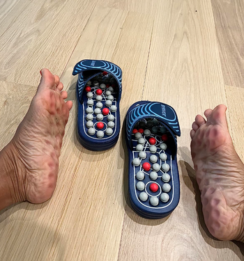 A person testing out acupressure slippers, with their feet resting beside them on the floor