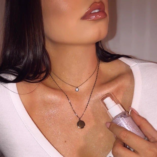 A model holding a bottle of shimmer oil, showcasing the radiant shimmer glistening on their collarbone.