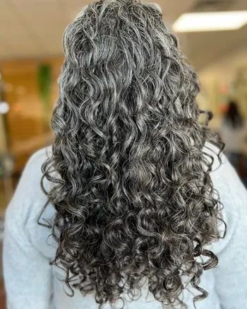 Close-up of a person with long, defined, curly hair cascading down their back, blending gray and dark tones beautifully.