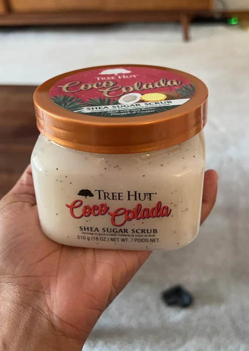 A person showcasing a close-up of the Tree Hut Coco Colada Shea Sugar Scrub jar, focusing on the front label.