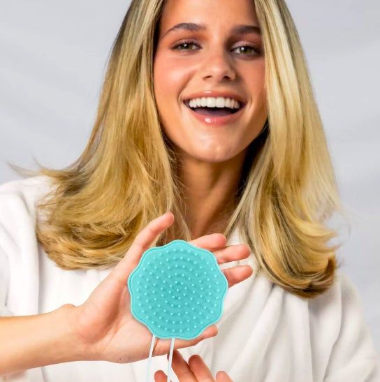 A model happily smiling while holding a blue facial cleansing brush in her hands.
