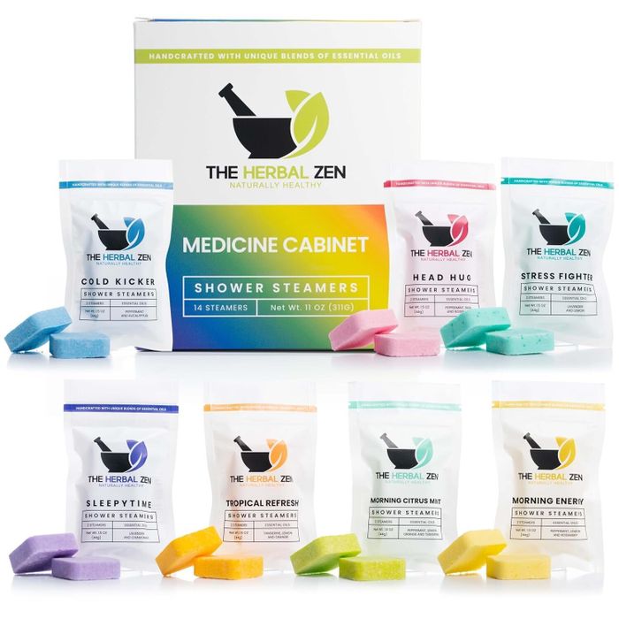 The image displays The Herbal Zen Medicine Cabinet shower steamers in a variety of scents, each individually wrapped in vibrant packaging.