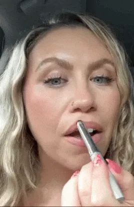 A reviewer applying lipstick in a close-up selfie video.