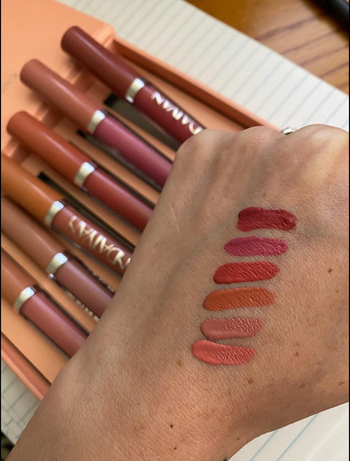 Reviewer showing off all six shades of pink and red matte lipsticks swatched on their hand.