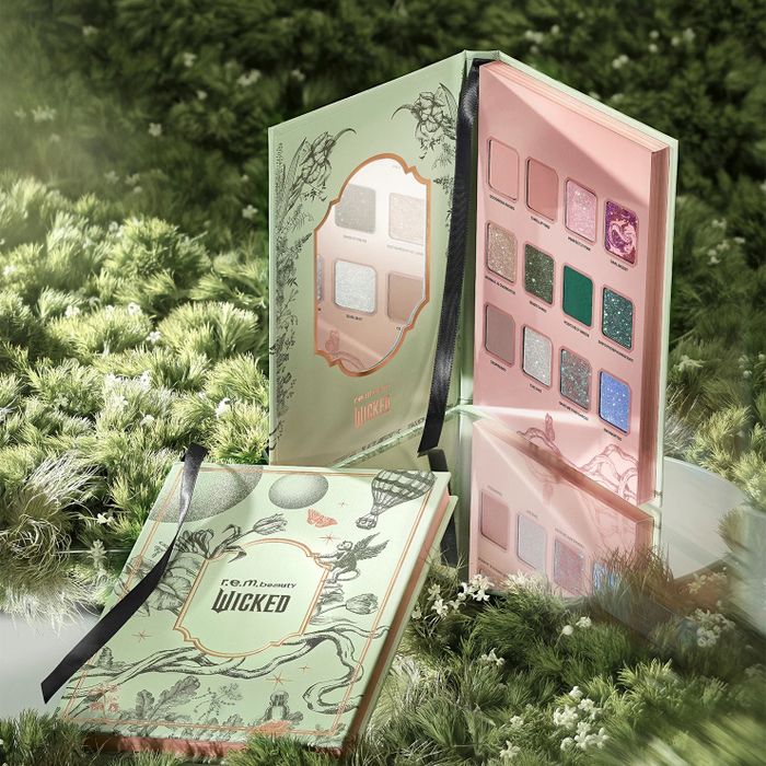 The open Wicked eyeshadow palette, displaying a variety of shades, placed on grass with another closed palette beside it.