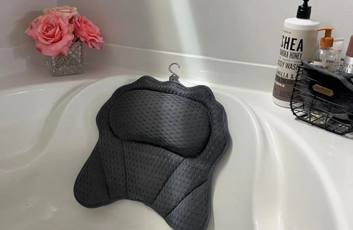 A bath setup adorned with pink roses in a vase, a cozy gray bath pillow, and a caddy holding various bath essentials, including SHEA body wash.