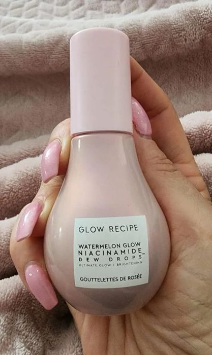 A hand holding a bottle of Glow Recipe Watermelon Glow Niacinamide Dew Drops, a perfect skincare addition for those seeking a radiant complexion