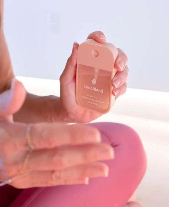Person holding a Touchland hand sanitizer, preparing to apply it with a smooth gesture.