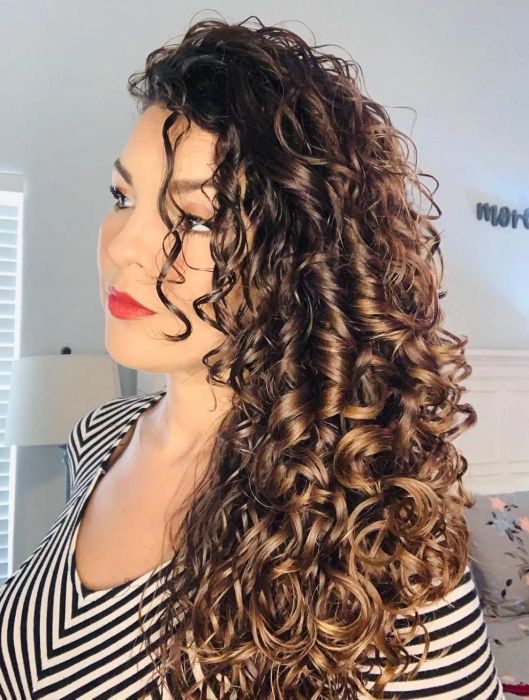 A person with voluminous curly hair, wearing a striped top, gazing sideways
