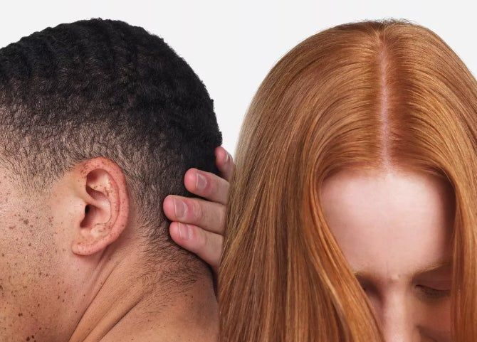 Close-up of two models standing back-to-back, both showing off their clear scalps. The person on the left has short hair, while the person on the right has long hair partially covering her face.