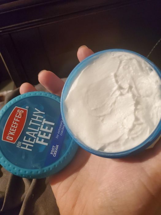 A hand holding an open jar of O'Keeffe's Healthy Feet Foot Cream, showcasing the cream inside