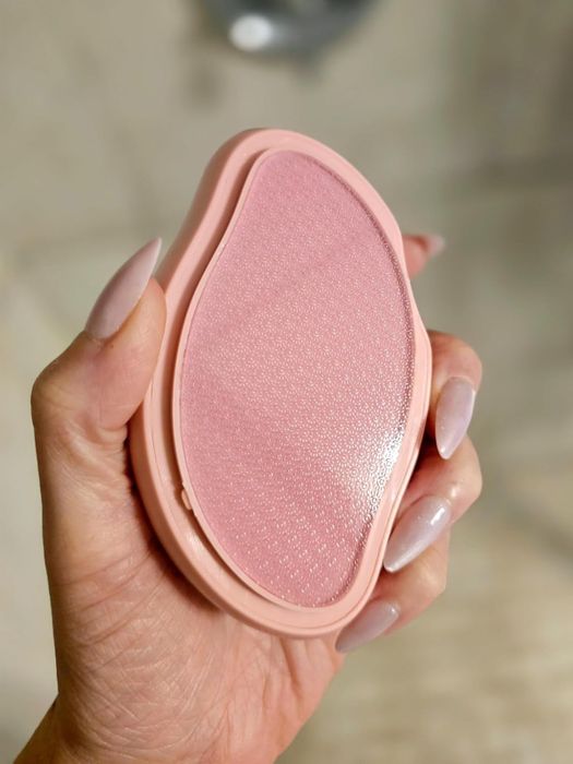 A hand holding a pink teardrop-shaped exfoliating foot file with a textured surface