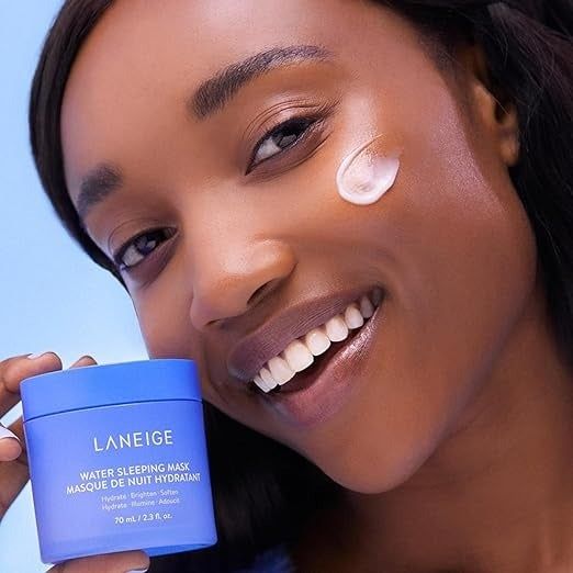 A person smiling with a small amount of Laneige Water Sleeping Mask applied to their cheek, holding the container next to their face.