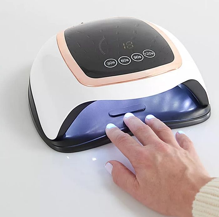 A hand inside a UV nail lamp, drying freshly painted nails. The lamp features four timer buttons on top for easy setting adjustments.