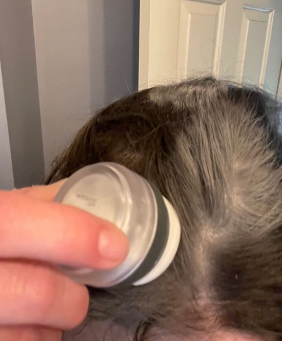A reviewer gently tapping the sponge onto their roots to apply the white powder