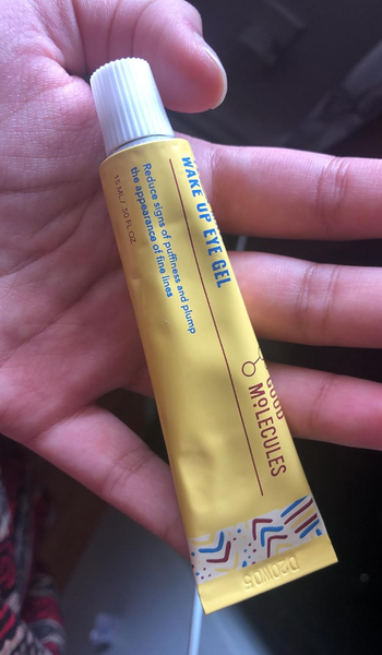A hand holding a tube of eye cream ready for application.