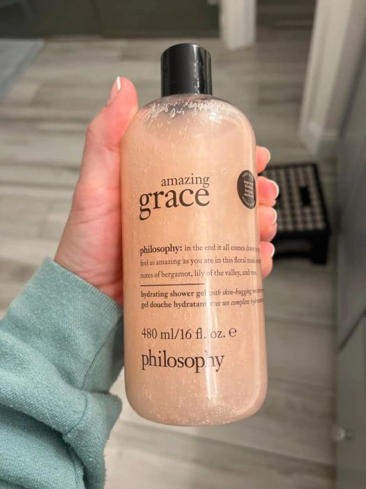 A hand holding a bottle of Philosophy Amazing Grace shower gel, 480 ml, infused with bergamot, lily, and musk fragrances.