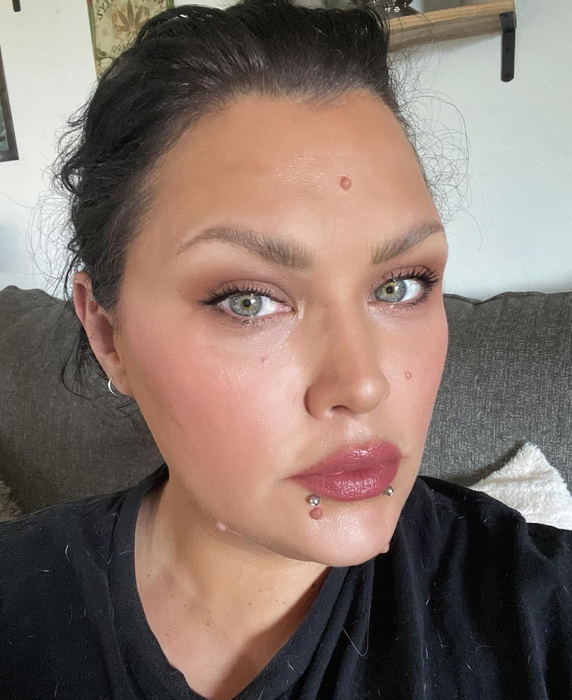 A person with dark hair and piercings, sporting a black shirt and showing off the shade of their blush.