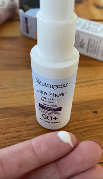 A hand holding the Neutrogena Ultra Sheer face serum with SPF 60+ bottle.