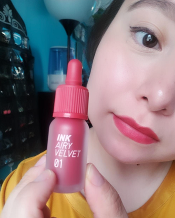 A reviewer rocking the reddish-pink lip tint while holding the bottle.