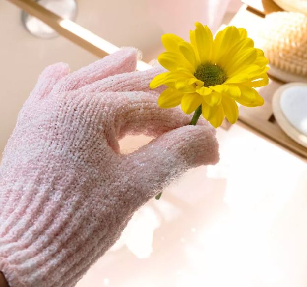 A hand wearing a soft, textured glove holds a yellow daisy, promoting a cozy, self-care product.
