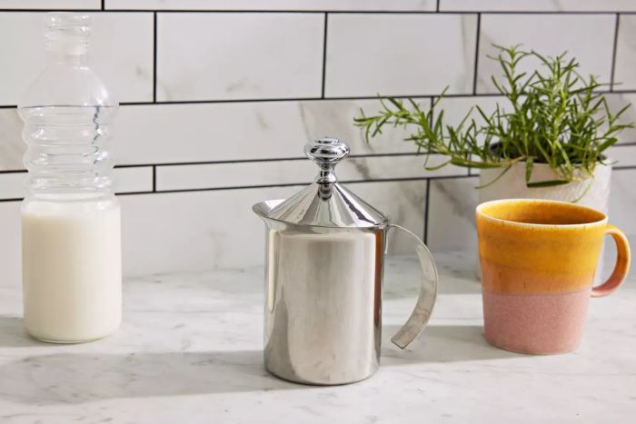 The HIC Fino Milk Frother placed on a counter with a carafe of milk and a mug beside it