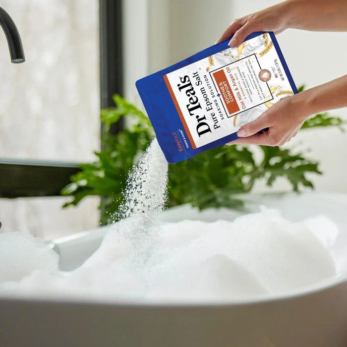 Dr. Teal's Epsom Salt being poured into a bubbly bath in a bright, airy bathroom.