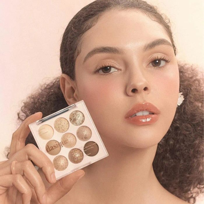 A person holding an eyeshadow palette with various hues, presenting a neutral makeup style