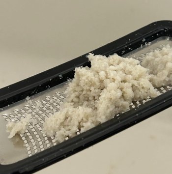 A close-up of dead skin collected on a metal foot file, ready for removal.