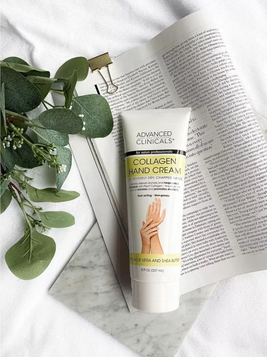 A tube of Advanced Clinicals Collagen Hand Cream resting on a magazine page, surrounded by green leaves
