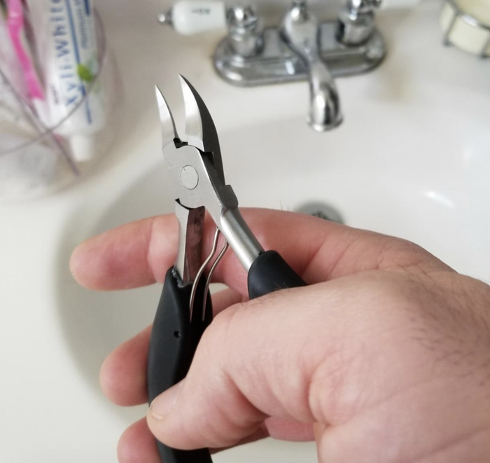 A reviewer holding the small, plier-like toenail clippers with sharp, pointed edges