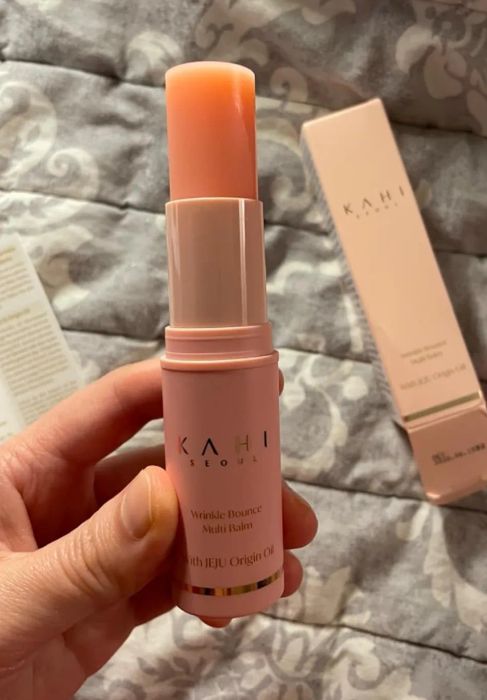 A hand holding the Kahi Wrinkle Bounce Multi Balm in front of its packaging