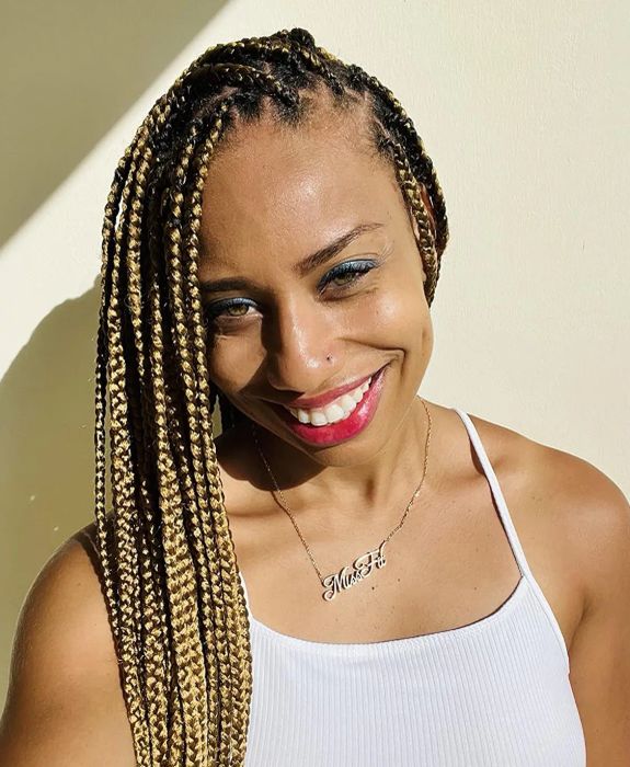 A woman with braided hair, smiling and wearing a tank top, showing off her look.