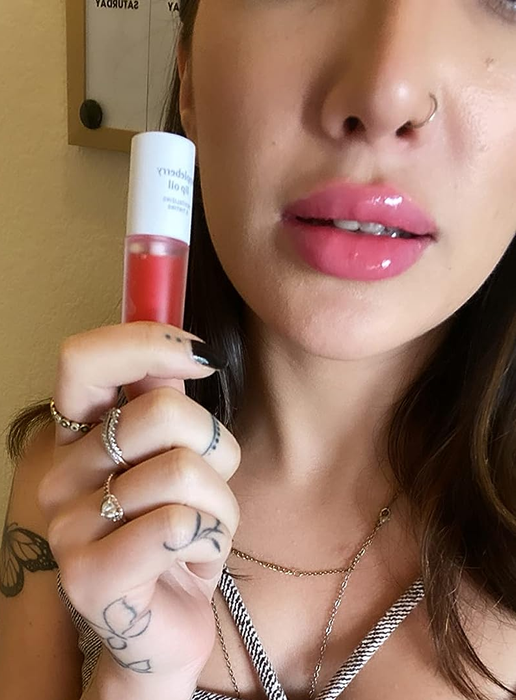 A reviewer holding the appleberry lip oil, with it applied to their lips