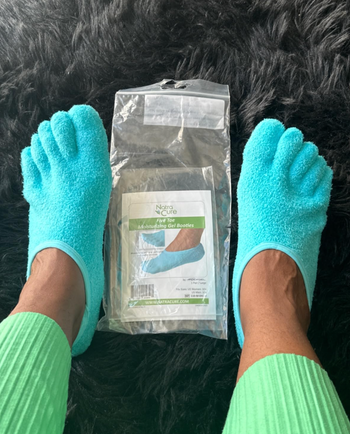 A person wearing turquoise moisturizing gel socks, with the product packaging placed on a furry surface