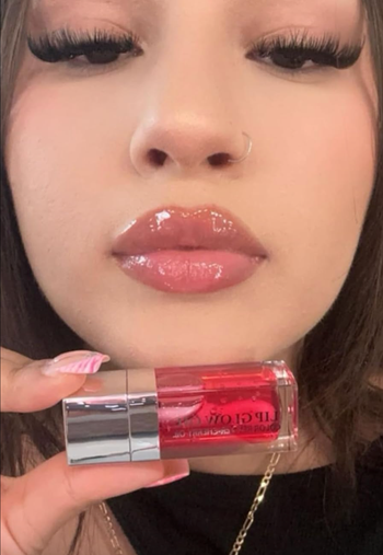 A close-up of a reviewer with glossy lips holding a tube of lip gloss.