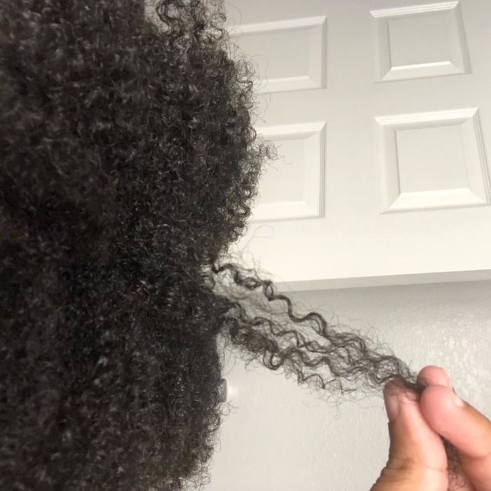 A reviewer with 4c hair holding a section of their hair to showcase how strong and hydrated their strands now look