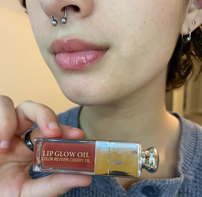A reviewer holding up a bottle of tinted lip oil.