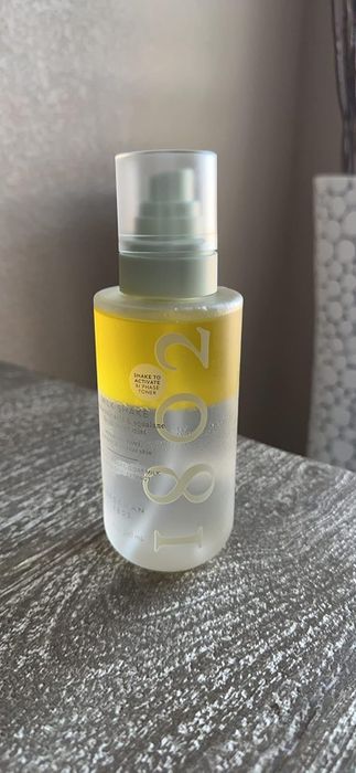 A skincare bottle with a frosted bottom and yellow liquid resting on a textured surface, displaying product details and name