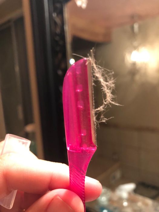 The reviewer holding up a pink dermaplaning razor with peach fuzz on it.
