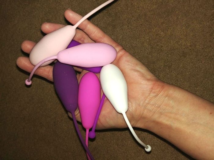 A reviewer's hand holding five different Kegel exercise weights in various shapes and sizes.