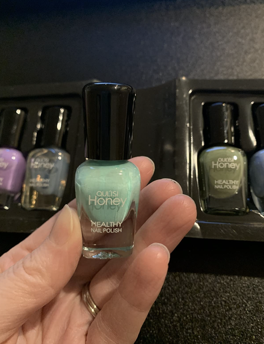 Reviewer holding a small bottle of blue nail polish, surrounded by other colors in the packaging