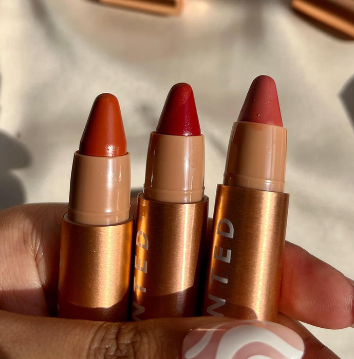 A hand holding several tubes of Huestick Corrector in three different shades.